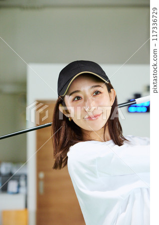 A woman practicing at an indoor golf driving range 117336729