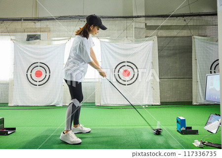 A woman practicing at an indoor golf driving range A woman practicing at an indoor golf driving range 117336735