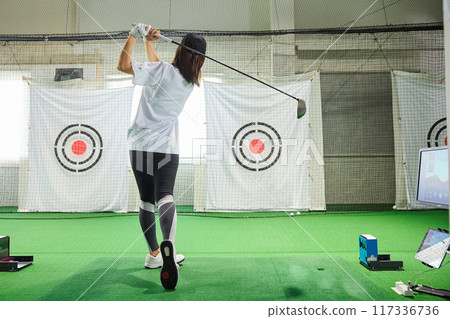 A woman practicing at an indoor golf driving range A woman practicing at an indoor golf driving range 117336736