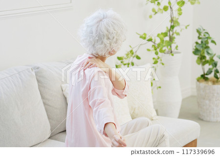 Back view of a senior woman with stiff shoulders in the living room Back view of a senior woman with stiff shoulders in the living room 117339696
