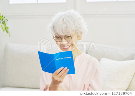 A senior woman smiling and looking at her medicine notebook A senior woman smiling and looking at her medicine notebook 117339704