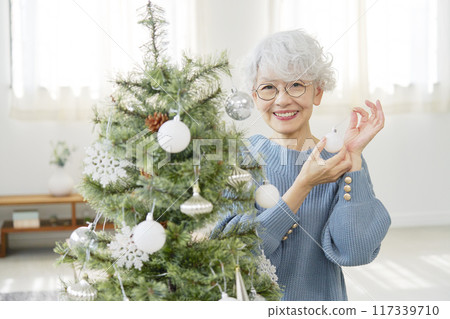 Senior woman decorating Christmas tree with ornaments Senior woman decorating Christmas tree with ornaments 117339710