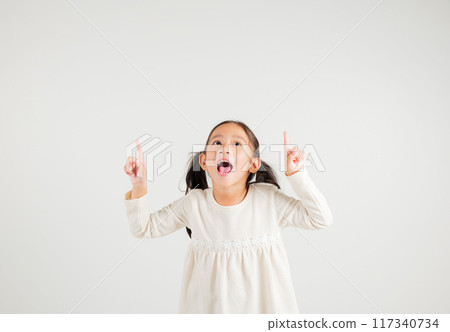 Asian happy portrait cute young kid girl makes gesture fingers point upwards above presenting product something, studio shot isolated on white background, kindergarten children woman smile 117340734