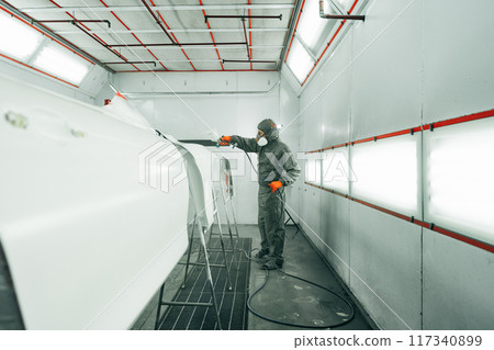 Auto painter painting a car with vaporizer gun inside a paint booth Auto painter painting a car with vaporizer gun inside a paint booth 117340899