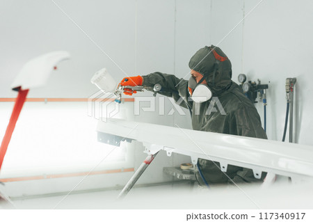Auto mechanic worker wearing protective workwear spraying white paint on car part at workshop Auto mechanic worker wearing protective workwear spraying white paint on car part at workshop 117340917