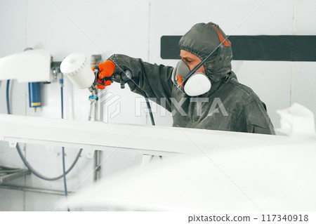 Male painter in respiratory mask and protective suit painting car with spray gun in car service Male painter in respiratory mask and protective suit painting car with spray gun in car service 117340918
