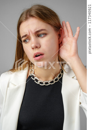 Woman in White Jacket Listening With Hand to Ear 117340921