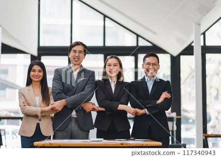 Four business professionals holding hands and smiling demonstrating teamwork and unity. 117340943