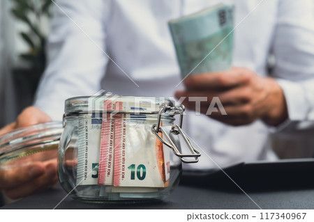 Euro Banknote Saving Money In Glass Jar. Unrecognizable man Moderate Consumption on calculator And Economy Collecting Money Tips Business Finance Euro Banknote Saving Money In Glass Jar. Unrecognizable man Moderate Consumption on calculator And Economy Collecting Money Tips Business Finance 117340967