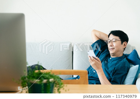 A man who uses a smartphone in the living room A man who uses a smartphone in the living room 117340979