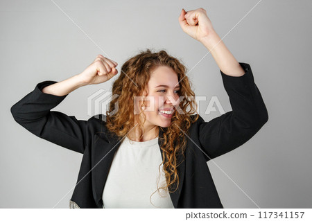 Joyful Young Woman Dancing Alone in Light-Colored Casual Attire Against a Grey Background 117341157