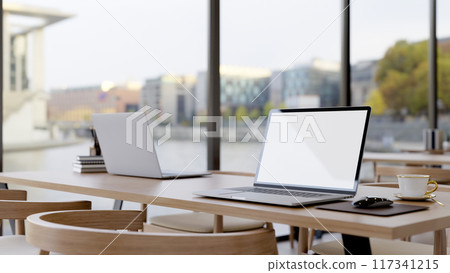 A laptop on a wooden table by the window, in a minimal contemporary coffee shop co-working space. A laptop on a wooden table by the window, in a minimal contemporary coffee shop co-working space. 117341215