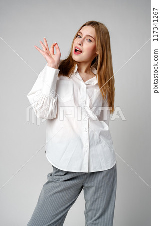 Young Woman Gesturing OK Sign With Hand Against a Neutral Background Young Woman Gesturing OK Sign With Hand Against a Neutral Background 117341267