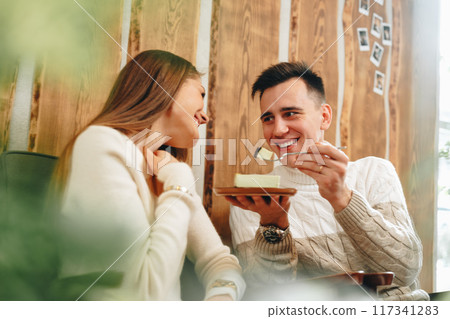 Young Man in White Sweater Enjoying Cheesecake With Friend at Cozy Cafe Young Man in White Sweater Enjoying Cheesecake With Friend at Cozy Cafe 117341283
