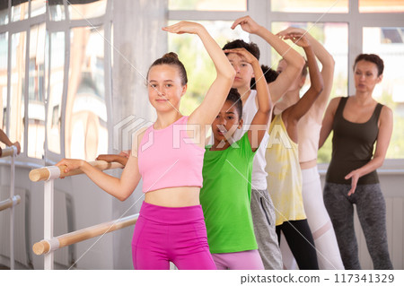 Teenage girl practicing battement tendu at ballet barre at group class 117341329