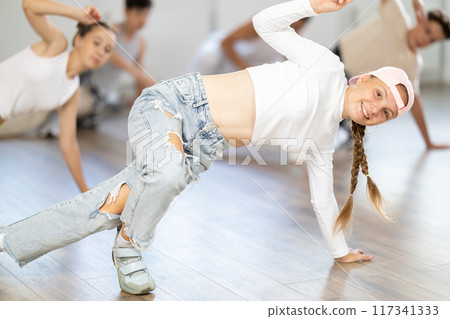 Girl in baseball cap with two hair pigtails with group of teenage friends, learn to dance hip hop Girl in baseball cap with two hair pigtails with group of teenage friends, learn to dance hip hop 117341333