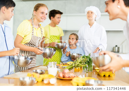 Tween girl listening to advices of professional chef during group cooking masterclass 117341446