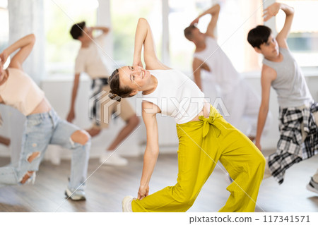 Teenage girl practicing hip-hop backbend moves in training hall 117341571