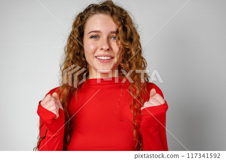 Excited Young Woman Celebrates Success With Raised Fists Against a Gray Background Excited Young Woman Celebrates Success With Raised Fists Against a Gray Background 117341592