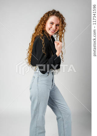 Excited Young Woman Celebrates Success With Raised Fists Against a Gray Background Excited Young Woman Celebrates Success With Raised Fists Against a Gray Background 117341596