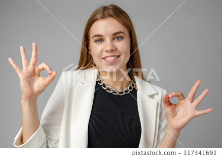 Confident Young Woman in Business Attire Giving Ok Sign in Studio Setting 117341691