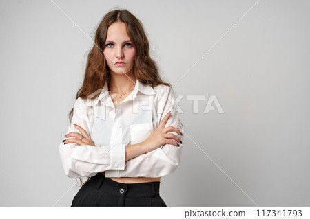 A woman is standing wearing a white shirt and black pants. She has a confident stance and is looking directly at the camera. 117341793