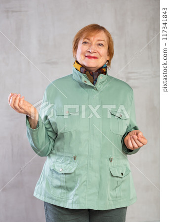 Smiling senior lady in light green jacket standing in studio 117341843