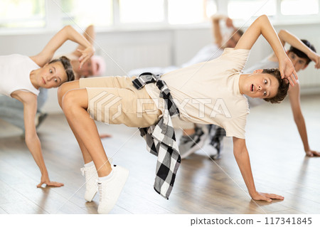Teen guy together with group of teenage friends, learn to dance hip hop in choreographic hall. 117341845