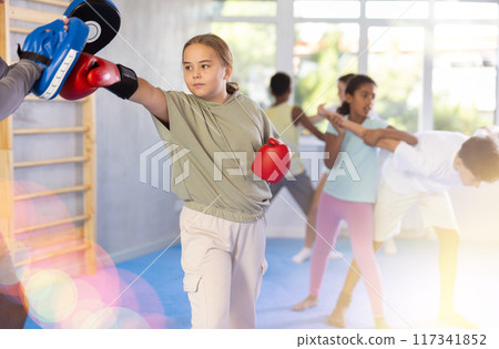 Focused girl hitting the focus mitts held by his boxing trainer in gym 117341852