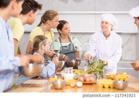 Professional female chef in white uniform conducting culinary class for tweens Professional female chef in white uniform conducting culinary class for tweens 117341921