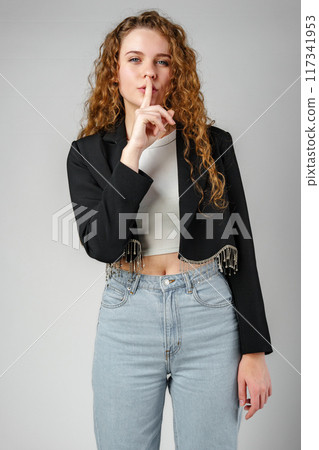 Young Woman Gesturing Silence With Finger on Lips Against a Grey Background Young Woman Gesturing Silence With Finger on Lips Against a Grey Background 117341953