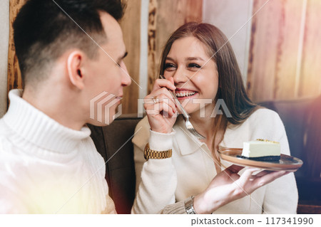 Young Man in White Sweater Enjoying Cheesecake With Friend at Cozy Cafe 117341990