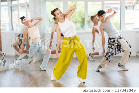 Team of teenagers rehearsing modern dances in dance hall Team of teenagers rehearsing modern dances in dance hall 117342049