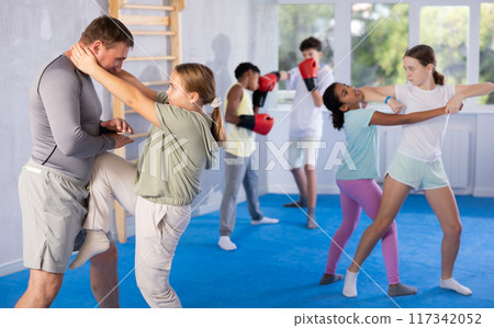 Tween girl performing knee strike in midsection to instructor in self-defense sparring 117342052