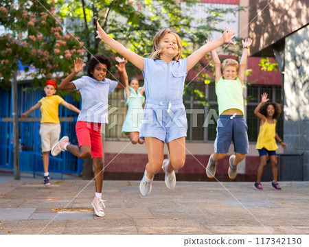 Cheerful preteen girl jumping with friends on summer city street 117342130