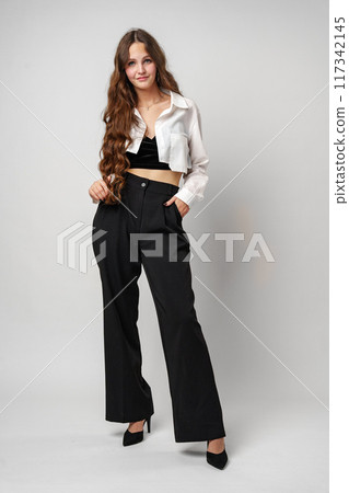 Confident Young Woman With Long Wavy Hair Posing in Casual Attire Against a Gray Backdrop 117342145