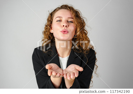 Young Woman Blowing a Kiss Towards the Camera in a Studio Setting 117342190