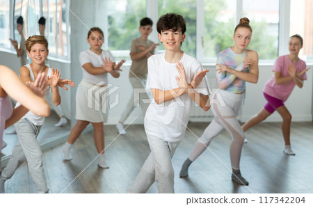 Male boy student repeats movements of unrecognizable teacher during group modern dance class. Male boy student repeats movements of unrecognizable teacher during group modern dance class. 117342204