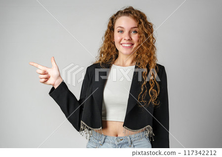 Smiling Young Woman Pointing While Posing in a Studio 117342212