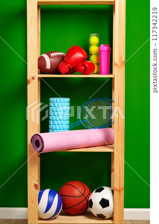 Shelves with different sports equipment against green wall Shelves with different sports equipment against green wall 117342219
