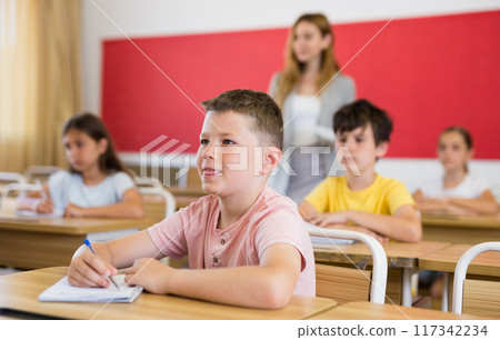 Smiling tween schoolboy sitting in classroom during lesson 117342234