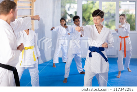 Determined tween boy practicing punches during group martial arts workout 117342292