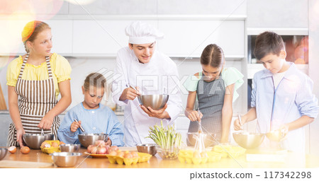 In cooking class, guy cook with bowl in hands tells children participants culinary ticks and tricks In cooking class, guy cook with bowl in hands tells children participants culinary ticks and tricks 117342298