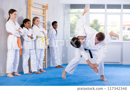 Jiu-jitsu coach demonstrating throws in training bout with teenager Jiu-jitsu coach demonstrating throws in training bout with teenager 117342348