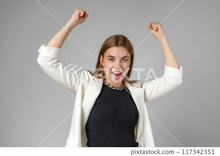 Confident Young Businesswoman Flexing Muscles in Smart Casual Attire Against Grey Background Confident Young Businesswoman Flexing Muscles in Smart Casual Attire Against Grey Background 117342351