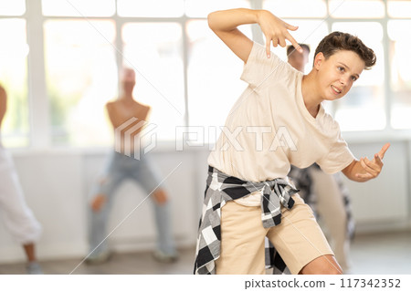 Group of sporty teenagers practicing hip hop dance in training hall during dancing classes Group of sporty teenagers practicing hip hop dance in training hall during dancing classes 117342352