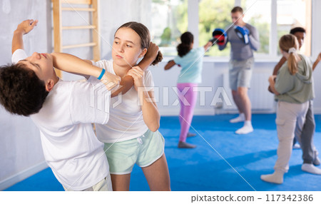 Girl practicing armlock with elbow strike to chin in mock bout with boy 117342386