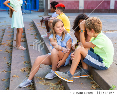 Group of boys and girls sitting on stairs outdoors and chatting Group of boys and girls sitting on stairs outdoors and chatting 117342467