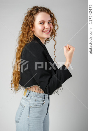 Excited Young Woman Celebrates Success With Raised Fists Against a Gray Background Excited Young Woman Celebrates Success With Raised Fists Against a Gray Background 117342473