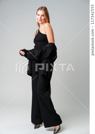 Young Woman Model in Black Top and Pants Posing on gray background Young Woman Model in Black Top and Pants Posing on gray background 117342555